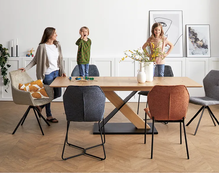 Moderner Holztisch mit Stühlen, zwei kleinen Kindern und einer langhaarigen Frau. 