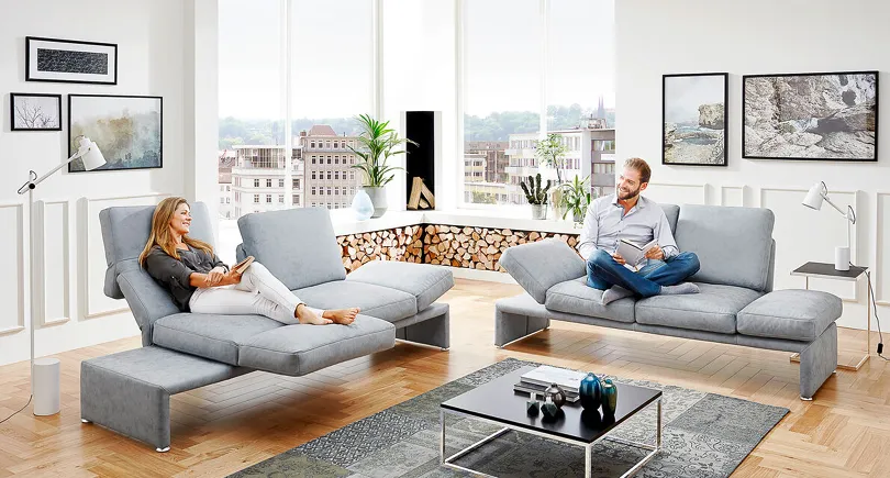 Graues Sofa mit drehbaren Sitzflächen im Wohnzimmer mit Holzboden, Mann und Frau auf moderner Couch