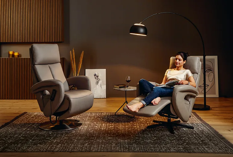 Frau im Relaxsessel im gemütlichen Wohnzimmer-Ambiete, barfuß auf Teppich am ergonomischen Relax-Sessel mit elektrischer Aufstehhilfe