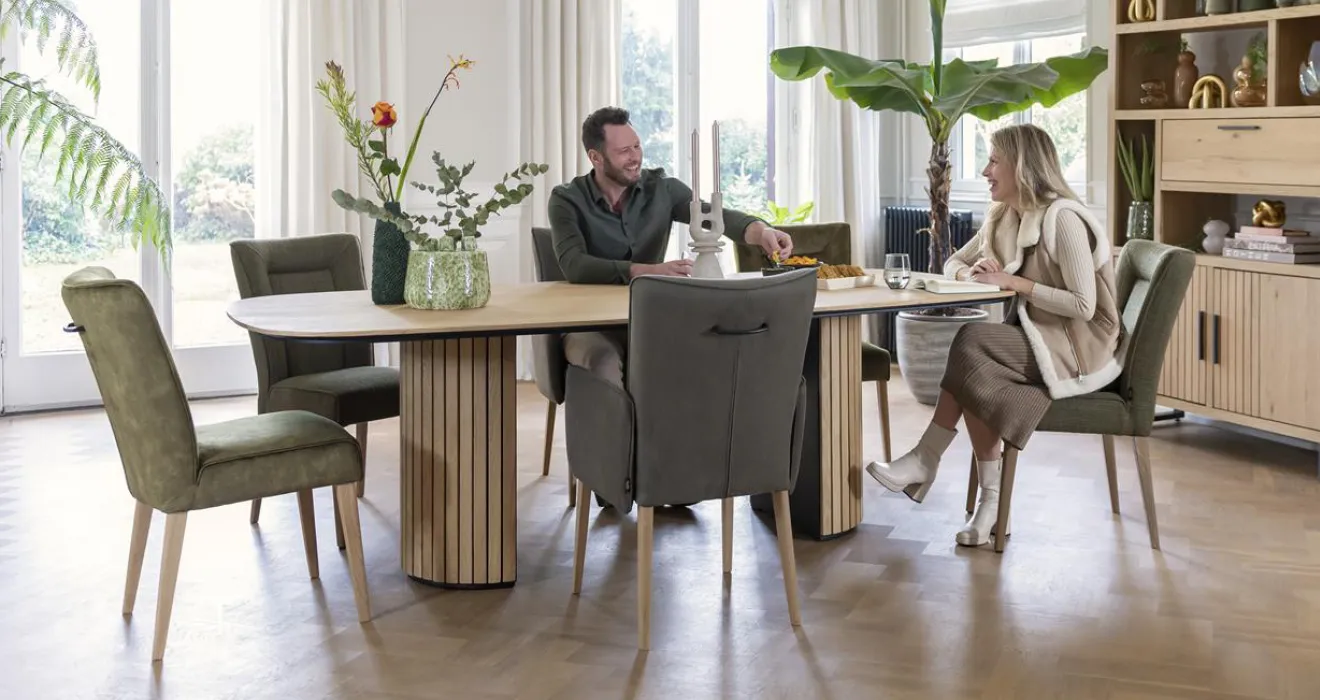 Sidboard aus Holz, Essbereich mit Tisch auf Metallgestell und hochwertigen Stühlen vor einer Treppe, Wohnbereich mit brauner Couch und Design-Couchtisch unter einer Zimmerdecke mit Holzbalken