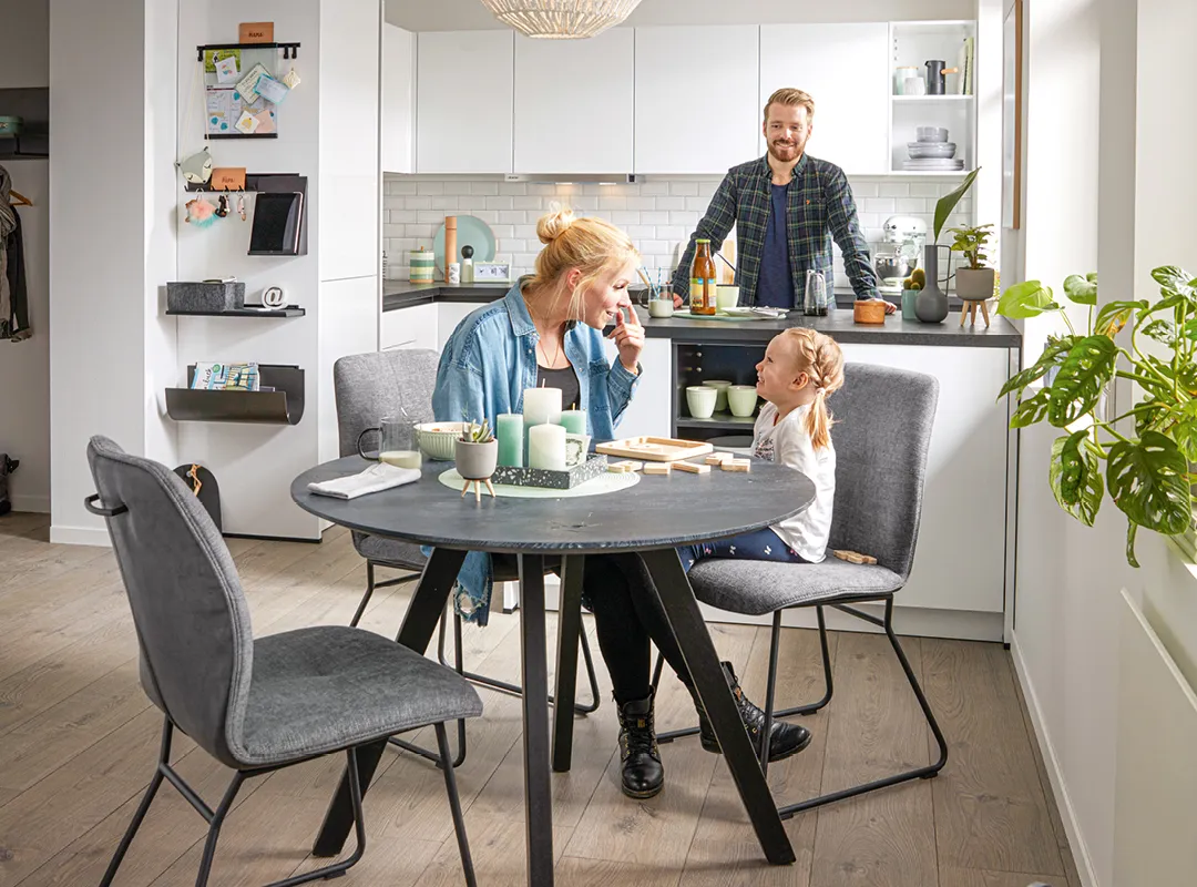 Vater, Mutter Kind am Esstisch bzw. an der Kochinsel in einer schwarz-weißen kompakten Wohnküche von Global Küchen