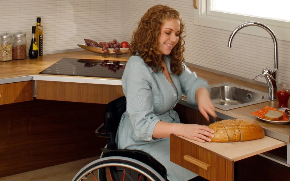 Frau im Rollstuhl kann dank Barrierefreier Küche alltägliche Aufgaben bewältigen.