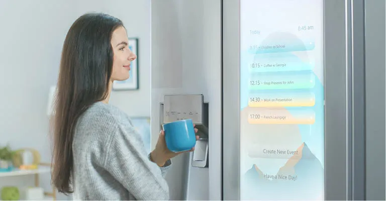 Eine Frau steht vor einem high-tech Kühlschrank mit Touchscreen und stöbert durch dessen Menü.
            