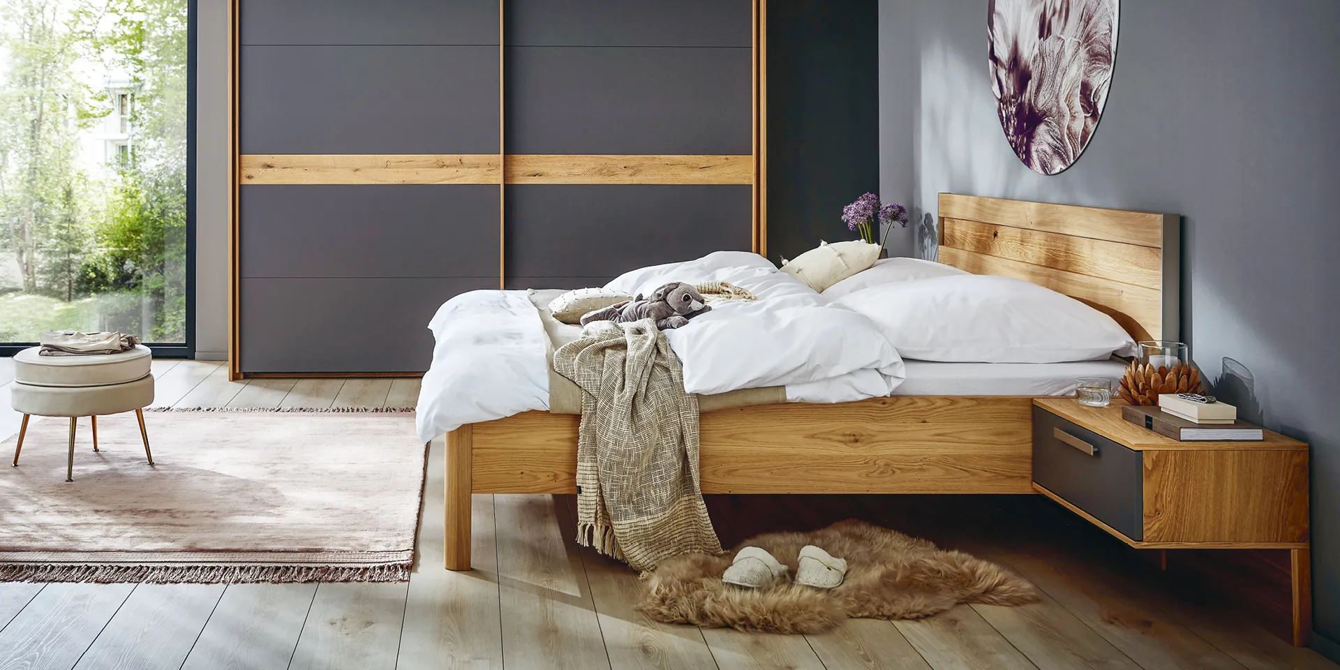 Bett, Nachttisch und Kleiderschrank im Schlafzimmer im modernen Materialmix aus Holz und dunklen Fronten