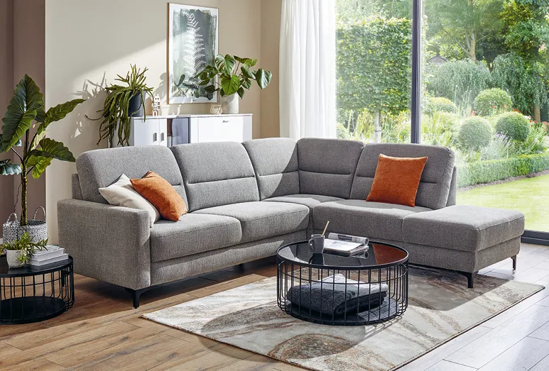 Graues Sofa, Global Merlos im Wohnzimmer mit beiger Wand und einem weißen Sideboard mit Grünpflanzen im Hintergrund