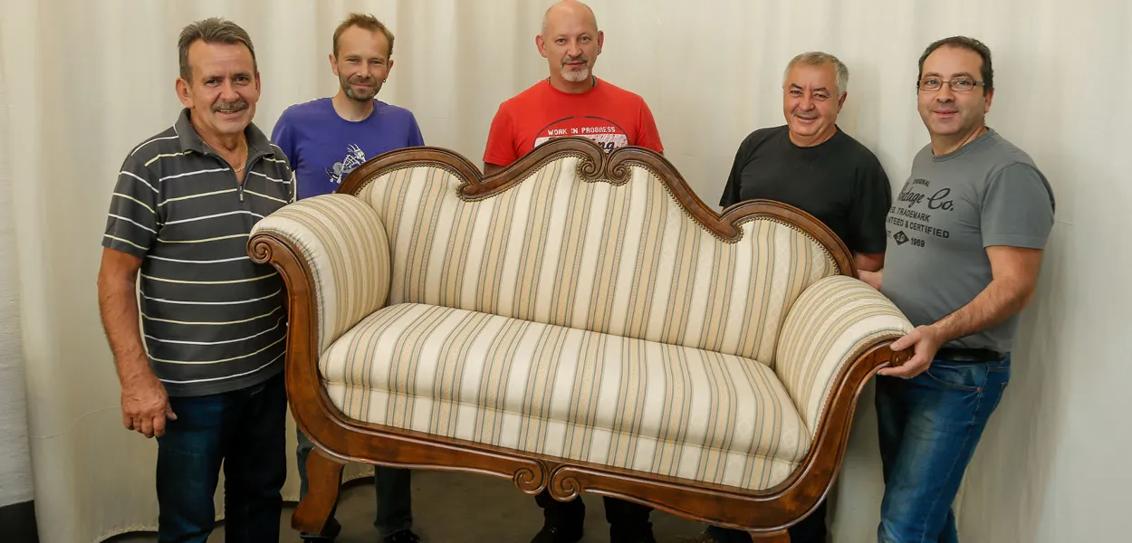 Fünf Männer halten restauriertes Polstersofa, Stuhl aus der Polsterei in Dortmund, Polsterer bei der Arbeit