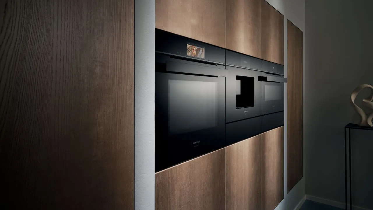 braune Küchenfront mit erhöht eingebautem schwarzem Backofen, daneben eingebaut ein schwarzer Kaffeevollautomat, nebenan ein schwarzer Backofen mit Mikrowellenfunktion
