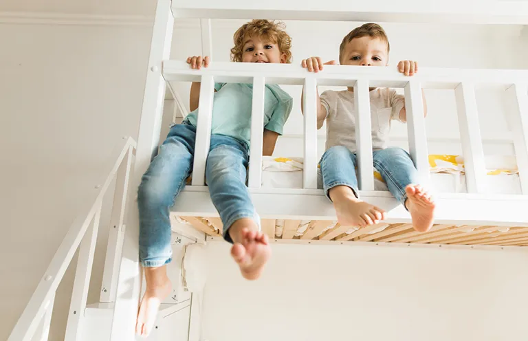 Zwei Jungen spielen auf einem weißen Hochbett im Kinderzimmer – clevere Einrichtung mit Hochbett für kleine Räume schafft zusätzliche Spielfläche und fördert kindgerechtes Wohnen.