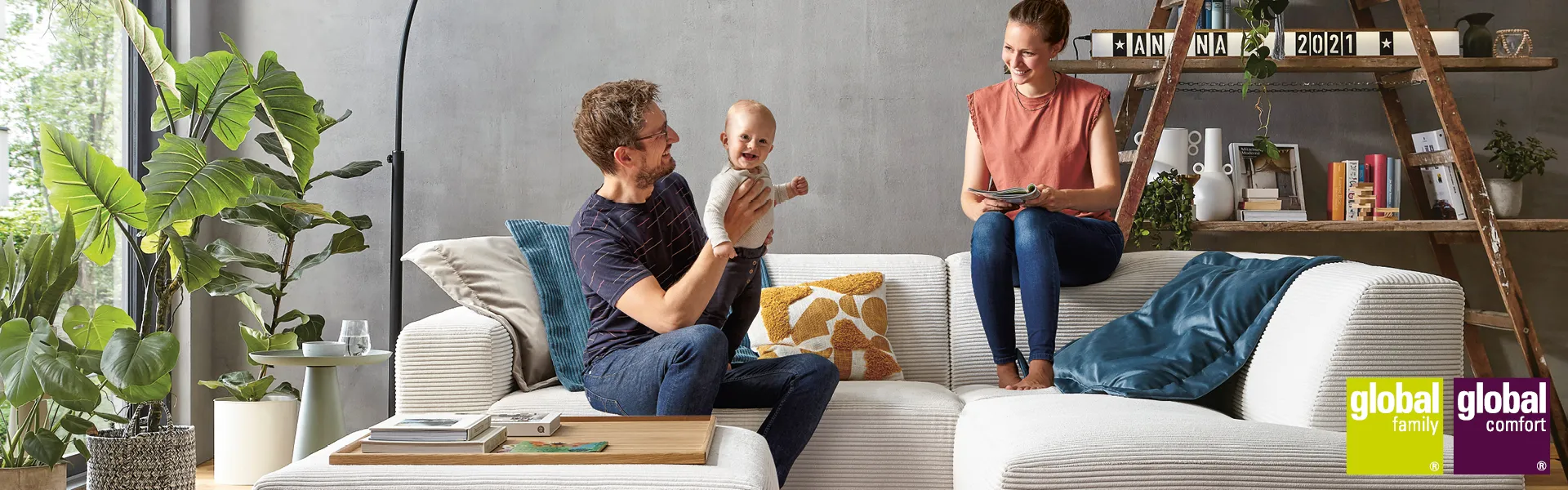 Frau und Mann mit Kleinkind auf einem modernen grauen Sofa im Wohnzimmer - gut gelaunt
