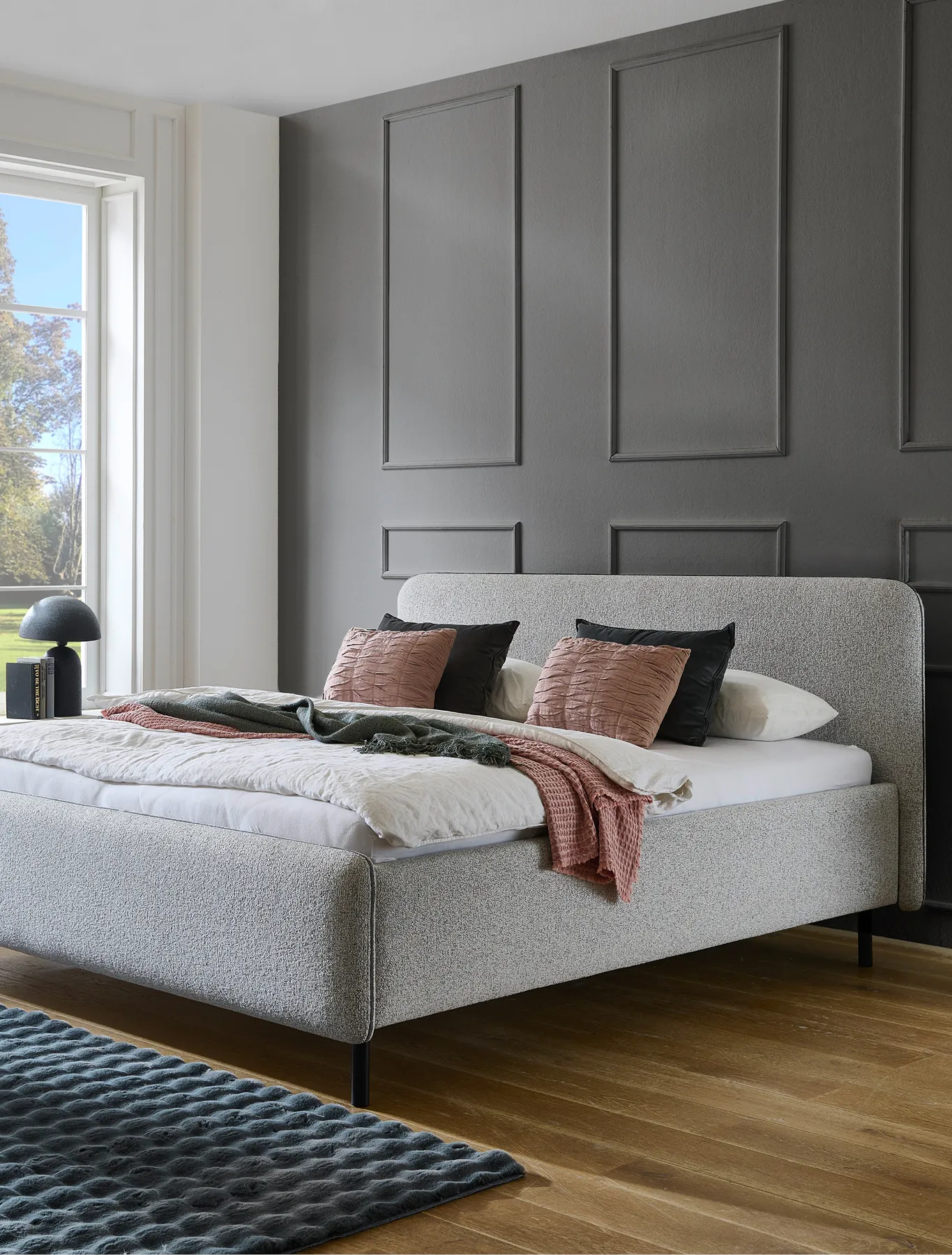 Gemütliches weißes Polsterbett neben großem Wandfenster