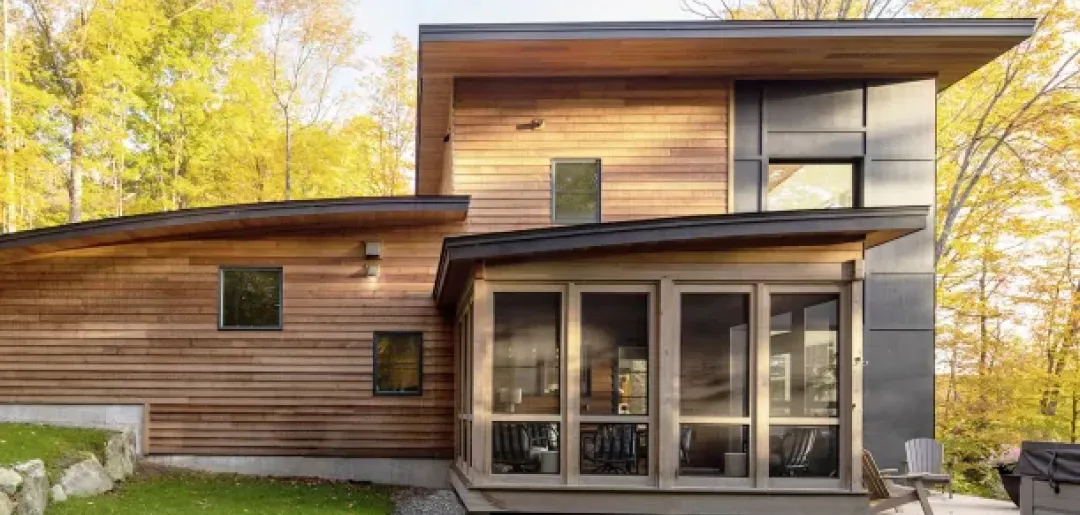 modernes Holzhaus mit Holzfenstern und Terrasse in sonnigem Wald
