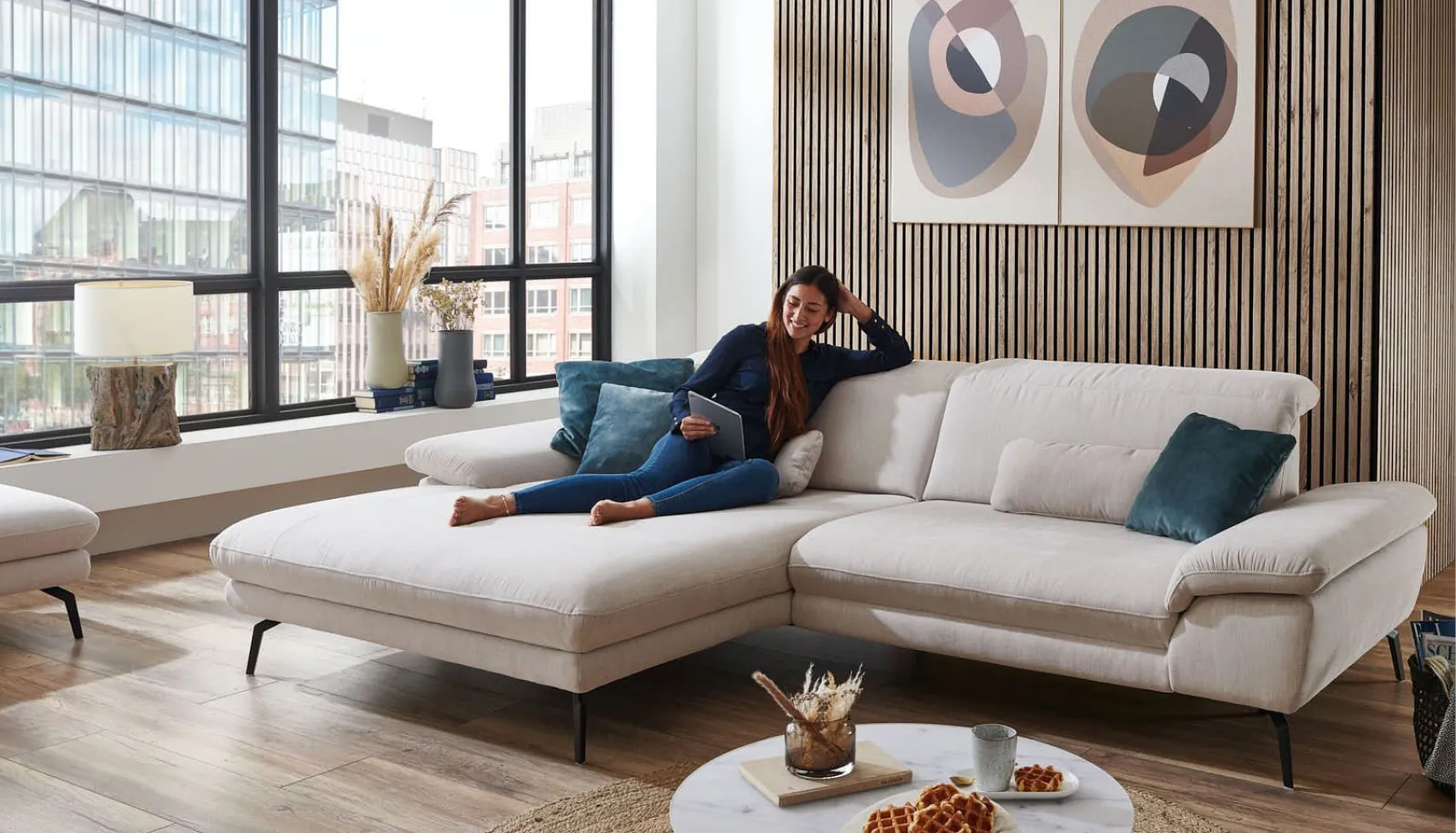 Frau sitzt auf großem Ecksofa und liest Möbelzeitschrift