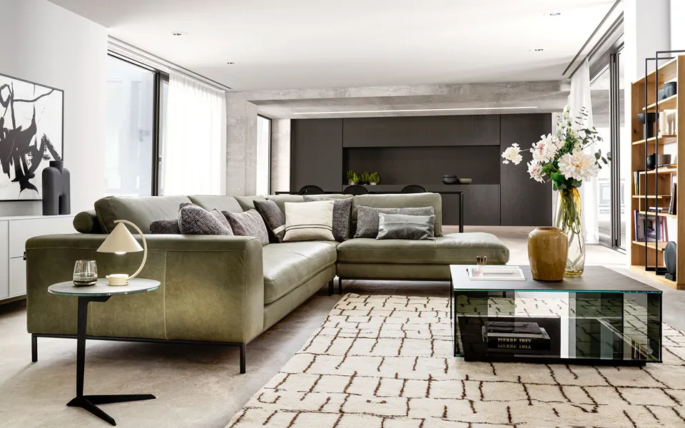 Wohnzimmer Ansicht mit Ledercouch in olivegrün und gläsernen Couchtisch.