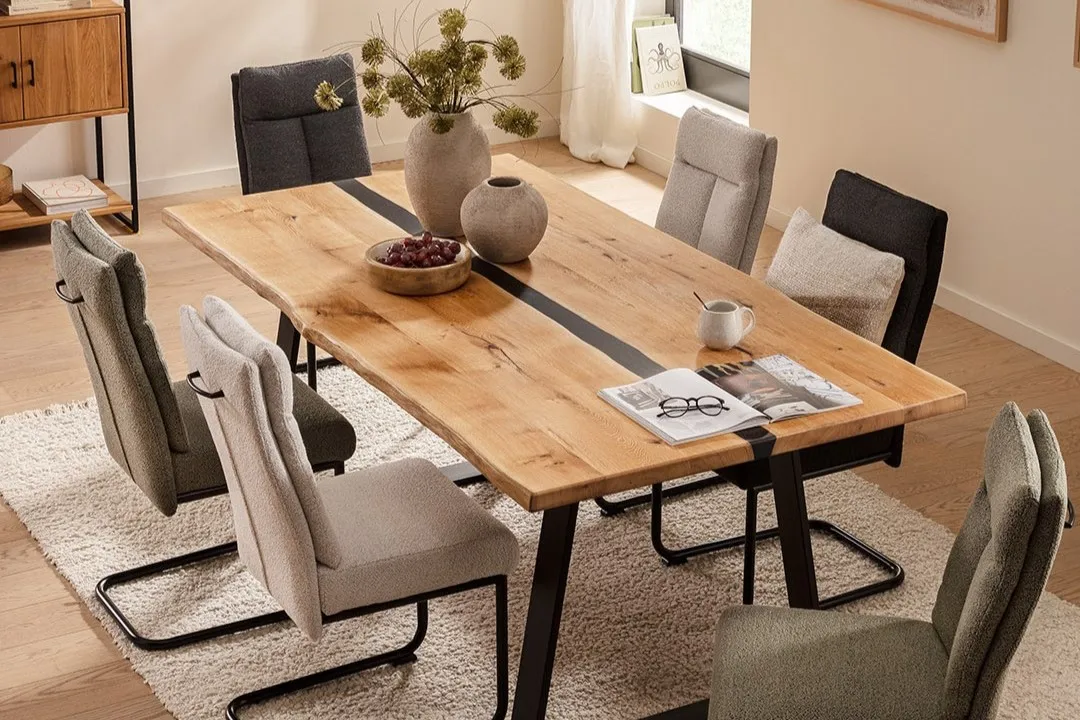 Esstisch mit Massivholzplatte und schwarzem Metallgestell mit einem schwarzen Element in der Tischplatte, um den Tisch herum Freischwinger in grau, beige und olivegrün.