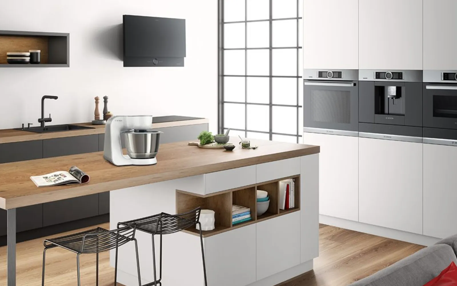 Moderne Küche mit Küchenzeile, Hochschränken mit Backofen, Kaffeemaschine und Dampfgarer und einer Kücheninsel. Weiße Fronten und Holzarbeitsplatten. 