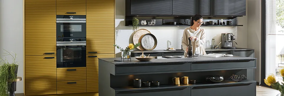 Frau in moderner Inselküche mit Einbaubackofen und Haengeschraenken