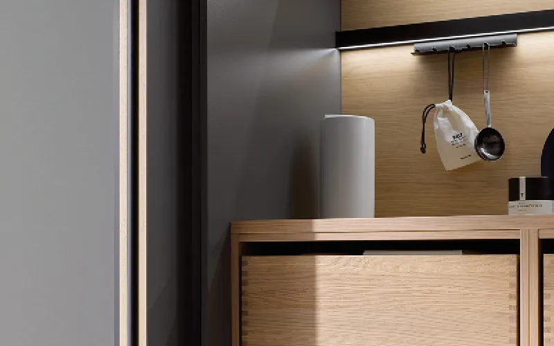 Detailansicht einer hochwertigen Küche mit Holzschubladen, offenen Regalen und integrierter LED-Beleuchtung. Kombination aus warmem Holz und modernen Grautönen für ein edles Küchenambiente.