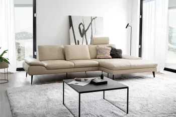 Beiges Ledersofa, bei dem eine Kopfstütze hochgeklappt ist in einem hellen Raum mit großen Fenstern.