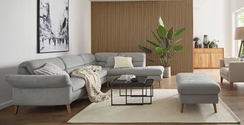 Graues Ecksofa dekoriert mit Kissen und Decke in Grau und Weiß, dazu ein passender Hocker und schwarze Beistelltische in einem modernen Wohnzimmer mit Akkustikpaneelwand.