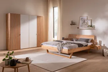 Helles gemütliches Schlafzimmer mit Kleiderschrank in hellem Holz mit Lamellenoptik und weißen Elementen an den Türen sowie ein dazu passendes Bett mit Lamellenoptik und weißen Elementen.