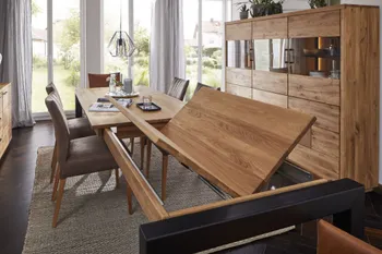 Esstisch aus Massivholz, bei dem gerade die Klappe zur Erweiterung ausgezogen wurde und wie bei einem Schmetterling ausgeklappt wird in einem gemütlichem Esszimmer mit Highboard aus Massivholz mit Glaselement.
