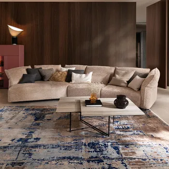 Beiges Designersofa, das trapezförmig verläuft, dekoriert mit mehreren Kissen in Beige, grau und weiß.