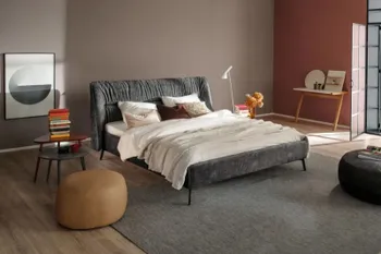 Graues Polsterbett in einem modernen Schlafzimmer, mit beigen, braunem und weißen Kissen und beiger und weißer Decke.