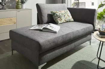 Graues Sofa mit Schlaffunktion, auf dem ein buntes Kissen und aufgeschlagenes Buch liegen in einem hellen Raum.