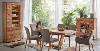 Esszimmertisch, Vitrine und Highboard aus Massivholz in einem gemütlichen Esszimmer, ein Mädchen sitzt am Esstisch vorm Laptop.