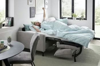 Ein Mann liegt auf einem gemütlichen grauen Schlafsofa, das zum Bett ausgezogen ist.