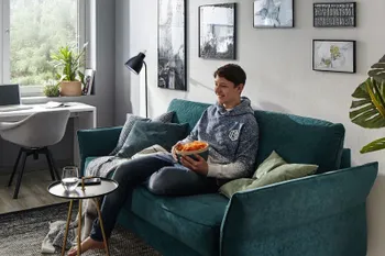 Petrolfarbenes Sofa mit leicht nach oben geklappter Armlehne, auf dem ein Junge sitzt in einem hellen Raum.