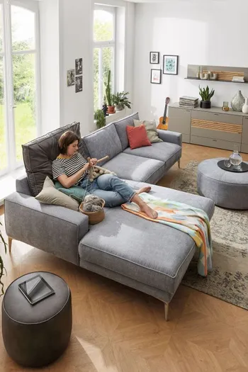 Gemütliches graues Ecksofa, auf dem eine Frau liegt.