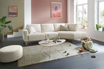 Beiges Ecksofa mit passendem runden Hocker in hellem und gemütlichem Wohnzimmer.
