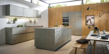 Graue Küche im Betonlook mit Kücheninsel samt in Holzwand eingearbeiteter Küchenzeile mit Einbaugeräten.