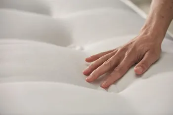 Matratze mit Knopfsteppung, auf der eine Hand liegt und über die Matratze streicht.