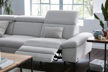 Hellgraues Sofa mit ausgeklappter Fußstütze und hochgestellter Kopfstütze in einem hellen Raum.