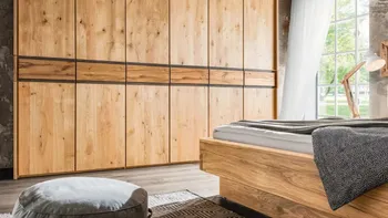 Großer Massivholzkleiderschrank mit sechs Türen, daneben ein Massivholzbett in einem Schlafzimmer mit Wänden im Industrial Look.