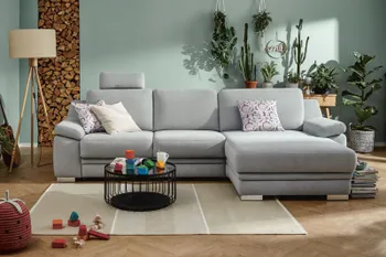 Graues Ecksofa, an der linken Sitzfläche ist eine Kopfstütze angebracht, auf der Sitzfläche liegen mehrere Kissen in hellen Tönen.