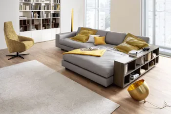Modernes Wohnzimmer mit einem gelben Relaxsessel mit Stoffbezug neben einem großen grauen Ecksofa mit gelben Kissen und Decken.