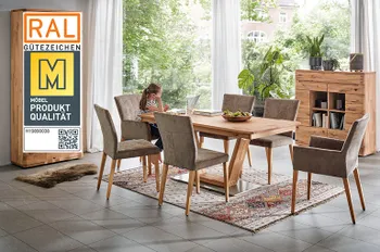 Qualitätssiegel &quot;Goldene M&quot; auf einem Bild von einem Esszimmertisch, Vitrine und Highboard aus Massivholz in einem gemütlichen Esszimmer, ein Mädchen sitzt am Esstisch vorm Laptop.