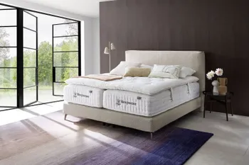 Boxspringbett mit beigem Boucle Bezug auf dem zwei Sleepeezee Matratzen liegen und ein Topper darauf und weiße und beige Kissen und eine Decke.