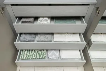 Drei geöffnete mit Kleidung befüllte graue Schubladen eines Kleiderschranks.