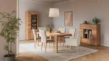 Esszimmer mit großem Esstisch aus Holz, passendem Highboard und Vitrine. Um den Esstisch gemütliche Stühle mit beigem Stoffbezug.