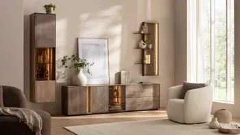 Moderne Wohnwand aus massiver Buche mit beleuchteten Glaseinsätzen in einem hellen Wohnzimmer, in dem ein heller Sessel, heller Teppich und helle Dekoration sind.