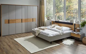 Kleiderschrank in grauem Lack und mit Elementen aus Naturholz neben einem Bett, dessen Rahmen in grauem Lack lackiert ist und Nachttisch und Kopfteil mit Massivholzelementen.