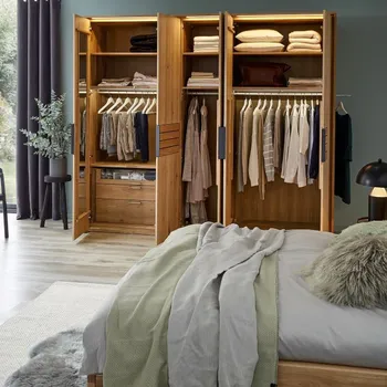 Drehtürenschrank aus Massivholz mit geöffneten Türen, mit Kleiderstangen, Schubläden und Regalböden die alle mit Kleidung belegt sind.