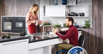 Person im Rollstuhl vollbringt normal Hausarbeiten an einer für Personen mit Handicap angepassten Küche.