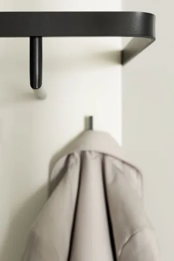 Weißes Brett modernen schwarzen Garderobenhaken, an einem Haken hängt eine beige Jacke.