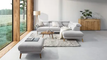 Weißes Ecksofa aus Cord mit passendem Hocker dekoriert mit weißen Kissen in einem gemütlichem hellen Wohnzimmer mit großer Fensterfront.