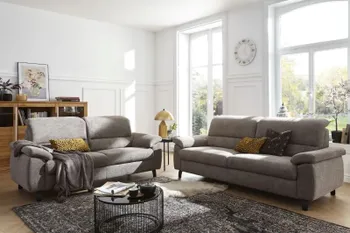 Zwei graue Sofas mit klappbaren Kopfstützen, die im rechten Winkel nebeneinander stehen in einem hellen gemütlichen Raum.